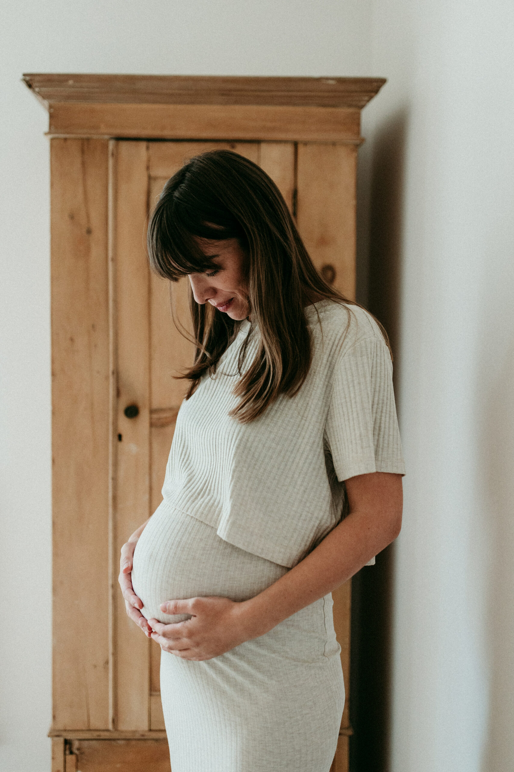 femme enceinte dans robe blanche devant armoire regarde son ventre